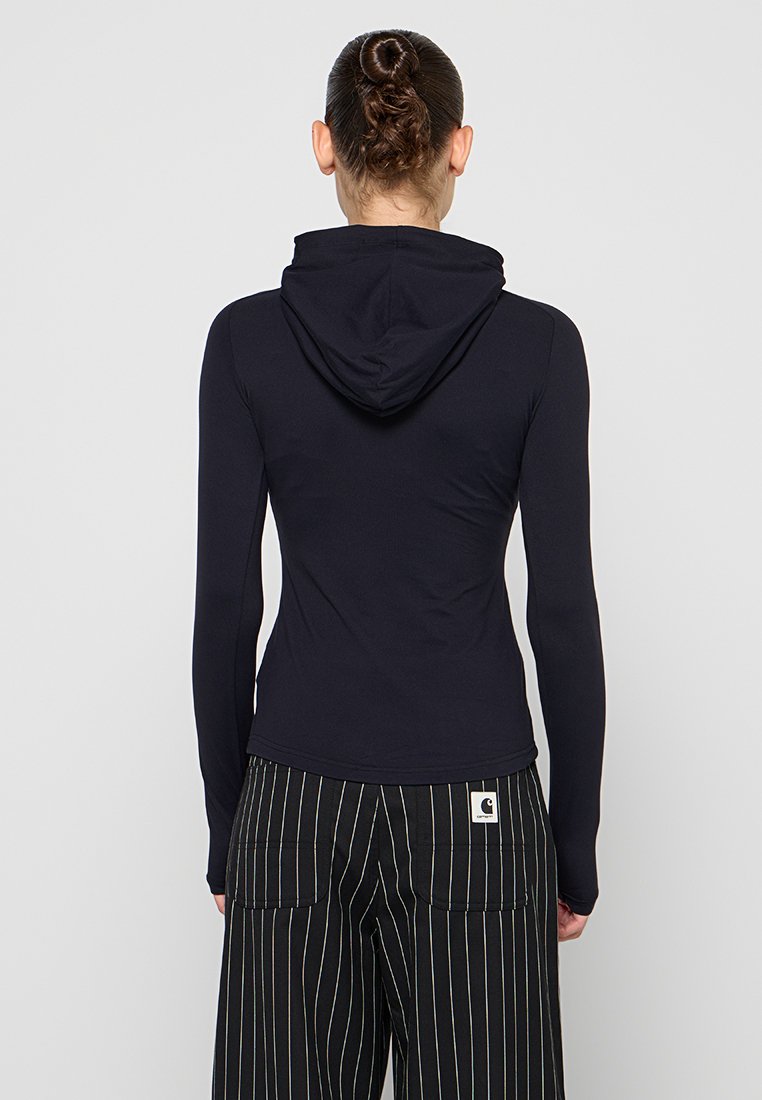 Navyblauer Hoodie mit langen Ärmeln und einer körperbetonten Passform, ausgestattet mit einer kleinen Kapuze hinten, kombiniert mit schwarz-weißen gestreiften Hosen. Glatte Stofftextur.