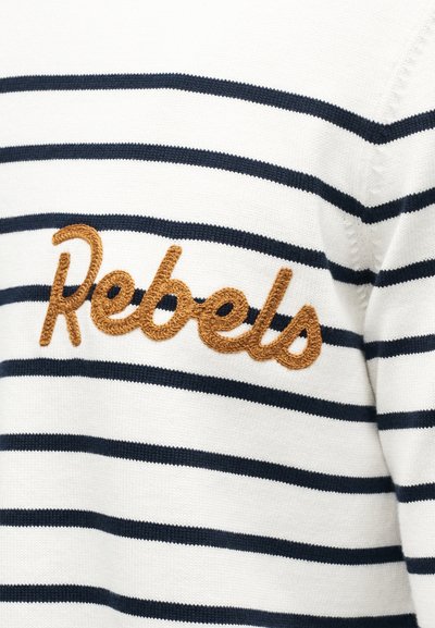 Tissu en maille blanche avec des rayures noires horizontales et le mot brodé "Rebels" en brun sur la zone de la poitrine d'un vêtement.