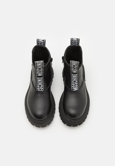 Botas de cuero negro hasta el tobillo con suela gruesa, cuentan con paneles laterales elásticos y tiradores de marca para facilitar su puesta. Diseño plano, textura suave.