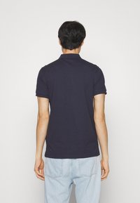 Navyblaues Poloshirt aus Baumwolle mit klassischem Kragen und kurzen Ärmeln, kombiniert mit hellblauen Jeans. Einfaches und lässiges Design.