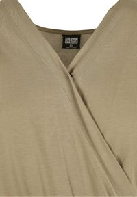 Vêtement beige à col en V avec tissu superposé et une étiquette noire au col indiquant "Urban Classics XS Made in China".
