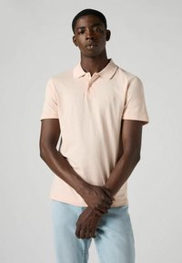 Ljust rosa pikétröja med klassisk krage och korta ärmar. Tillverkad av mjukt material, har en liten logotyp på bröstet. Bärs med ljusblå jeans.