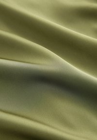 Alyvos žalios satino medžiaga su lygiu, blizgiu tekstūru. Pasižymi švelniais klostėmis ir šiek tiek spindesiu, pabrėžiančiu jos turtingą spalvą ir medžiagą.