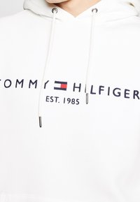 Felpa bianca con cappuccio in cotone, caratterizzata da una grafica frontale in navy e rosso con il testo "TOMMY HILFIGER" e la data di fondazione, con cappuccio regolabile.