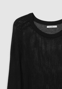 Maglione nero lavorato a maglia con un design a trama aperta e morbida. Presenta un collo rotondo e maniche lunghe. Tessuto testurizzato con un leggero luccichio.