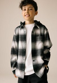 Chemise à carreaux noir et blanc à boutons avec capuche, en tissu doux, accompagnée d'un t-shirt blanc contrastant en dessous, assortie à un short sombre.