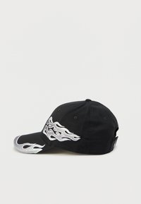 Czarna czapka z haftowanym srebrnym płomieniem po boku. Posiada zakrzywiony daszek i otwory wentylacyjne na koronie.