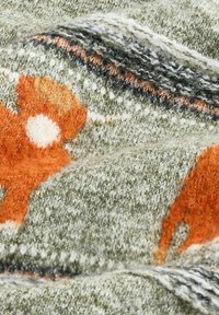 Pletená látka s jemným, textúrovaným povrchom v zelenej farbe, pričom obsahuje oranžové a biele abstraktné vzory a čierne a krémové pruhy.