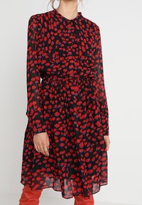 Black dress with red and blue floral pattern, long sleeves, collar, gathered waist, and flowing silhouette. Sheer texture and knee-length.