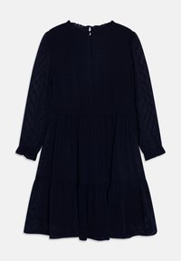 Marinblå klänning med långa ärmar, texturerad tyg med små prickar, volangärmar och en nyckelhålstängning i ryggen med en knapp.