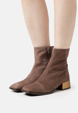 Bottines en daim marron avec un bout arrondi, une fermeture éclair sur le côté et un petit talon bloc doré. Présente des détails de couture subtils sur le bout.