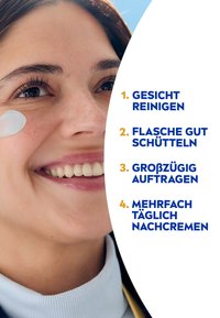 Eine Frau trägt eine Creme auf ihre Wange auf; sie hat dunkles Haar und einen hellblauen Rollkragenpullover. Der Hintergrund ist hell mit blauem Himmel. Text in Deutsch erscheint.