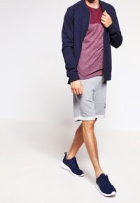 Marinblå zip-jacka, vinröd och grå mönstrad skjorta, grå shorts och marinblå sneakers. Lätta och ventilerande material, avslappnad atletisk stil.