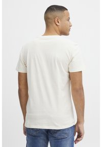 Lys beige bomuld t-shirt med rund hals og korte ærmer, vist fra ryggen. Bærer den med blå denim jeans. Enkel, ensfarvet design.