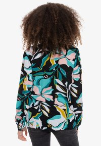 Camicia a maniche lunghe con sfondo nero caratterizzata da motivi floreali colorati in rosa, verde e giallo; tessuto strutturato con polsini arricciati.