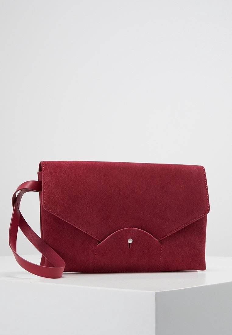 Bordó semišová kabelka s překlopným uzávěrem, kulatým dnem a malým kovovým patentním detailem. Obsahuje odpovídající ramenní popruh.