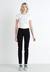 Sorte denim skinny jeans med mid-rise liv, kombinert med en tettsittende hvit t-skjorte og lyseblå sneakers; minimalistisk design og tekstur.