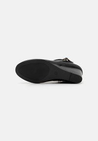 Suela de zapato negra con un patrón texturizado, que presenta un ligero tacón y una punta redondeada. Material suave con un diseño minimalista y un logo.