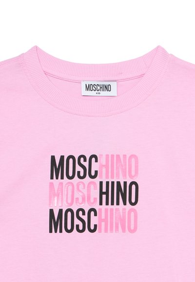 Ροζ παιδικό μπλουζάκι με στρογγυλή λαιμόκοψη και ριμπε ύφασμα, με επαναλαμβανόμενο κείμενο "MOSCHINO" σε μαύρο και ροζ στο μπροστινό μέρος.