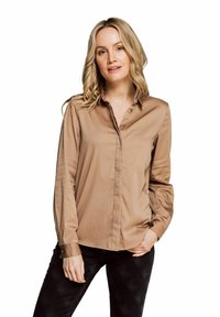 Light brown button-up shirt with long sleeves, a collar, and smooth texture. Paired with dark jeans, showcasing a tailored fit.