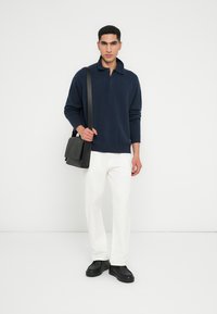 Pullover blu navy, vestibilità rilassata, con colletto. Abbinato a pantaloni bianchi e sneakers nere. Borsa a tracolla nera con dettaglio a patta.