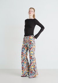 Top a maniche lunghe nero abbinato a pantaloni a palazzo flared con un motivo colorato e vorticoso. Tessuto leggero, colori vivaci e una texture liscia.