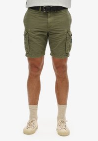 Pantalones cortos cargo de color verde oliva con múltiples bolsillos laterales, costuras cosidas y un corte relajado, combinados con zapatillas beiges y calcetines de color claro.