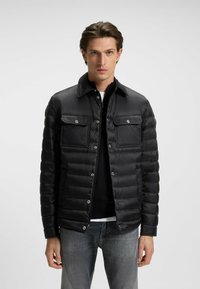 Svart pufferjacka med krage, försedd med två bröstfickor och tryckknappsstängning. Slät textur och kviltat mönster.