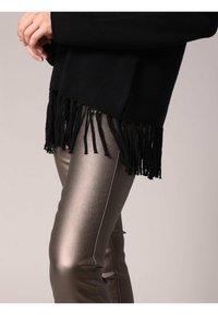 Zwarte trui met franjes aan de onderkant, gemaakt van zachte garen, gedragen over glanzende metallic strakke broek met een witte zijstreep.