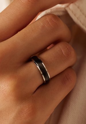 Schwarzer und silberner Ring an einer Hand; besteht aus einem glatten schwarzen Band mit einer silbernen Kante. Die Fassung ist poliert und hat ein elegantes Design.