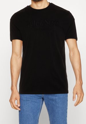 Schwarzes Baumwoll-T-Shirt mit kurzen Ärmeln, einem geprägten Logotext und einem Rundhalsausschnitt, kombiniert mit hellblauen Denim-Jeans.