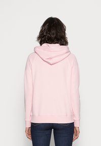 Różowa bluza z kapturem, z prążkowanymi mankietami i dołem, o luźnym kroju i miękkiej fakturze, widziana z tyłu.