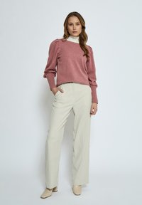 Pink cropped sweater with puffed shoulders, paired with cream high-waisted trousers and beige ankle boots. Smooth texture and fitted design.