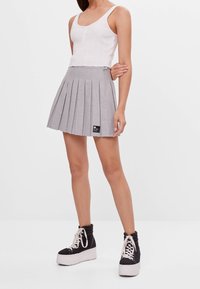 Šedá plisovaná sukně s texturovaným vzorem, kombinovaná s bílým krátkým topem. Černé platformové tenisky s bílými podrážkami a tkaničkami.