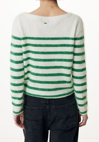 Grön och vit randig tröja med en lös, båtformad halsringning. Tillverkad av mjukt, fluffigt material. Matchad med mörka jeans med bakfickor.