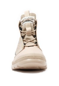 Beżowy wysoki sneaker z teksturowaną podeszwą, pętelką do wciągania, czarnymi elastycznymi sznurówkami i widoczną metką na języku na białym tle.