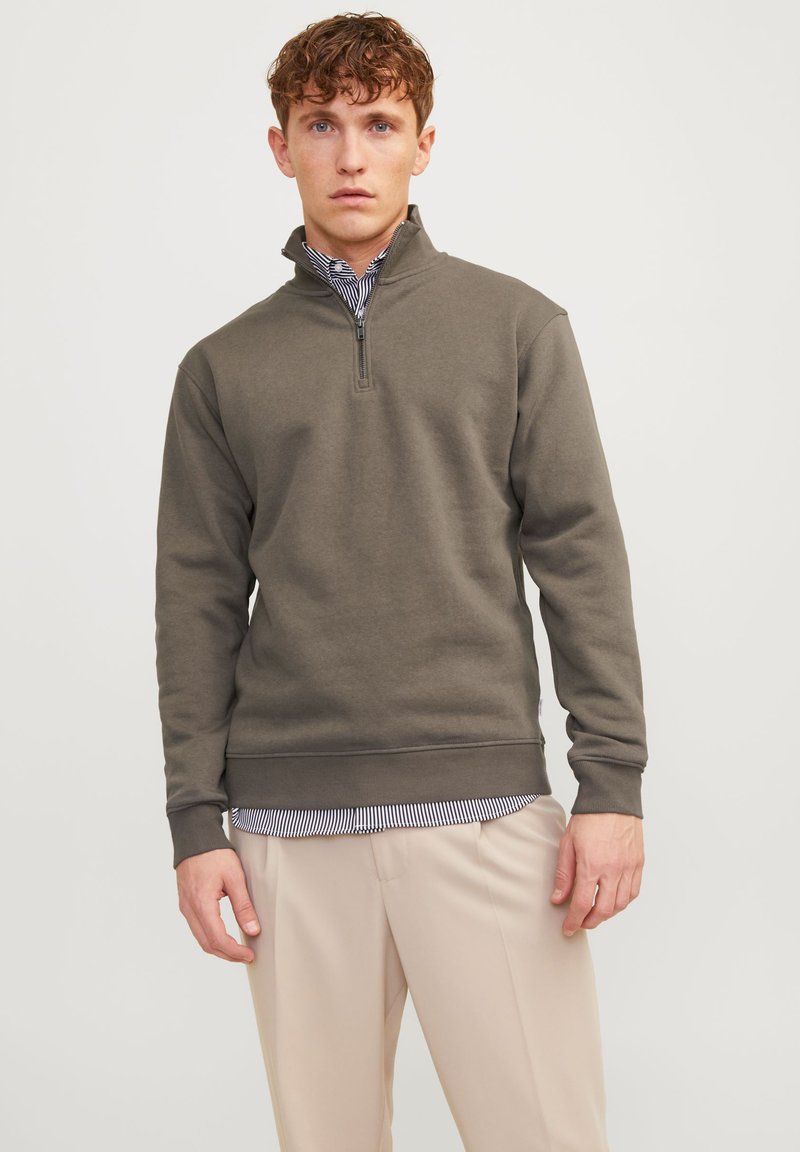Donker groene quarter-zip sweatshirt van zacht materiaal, met lange mouwen en geribde manchetten, gecombineerd met een gestreept shirt en lichte broek.