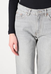 Lys grå denimjeans med høy midje, femlommedesign og beslag i kobberfarge. Har rett ben og lett falming for tekstur.