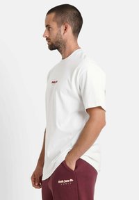 Witte katoenen t-shirt met korte mouwen, met een rood tekstlogo aan de voorkant. Gecombineerd met bordeauxrode sweatpants met witte logodetails.