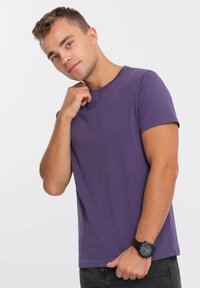 Lilla kortærmet t-shirt lavet af bomuld, med rund hals og en afslappet pasform. Bæres med sorte jeans og et sort armbåndsur.