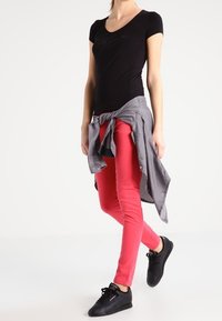 Czarny t-shirt z krótkim rękawem i dekoltem w serek, czerwone obcisłe dżinsy, szara koszula związana w talii, czarne tenisówki. Prosty design bez widocznych wzorów.