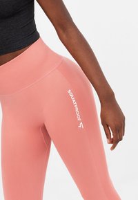 Leggings rosa opachi con texture a coste, fascia alta in vita e logo bianco stampato su un lato. Design elasticizzato e aderente.
