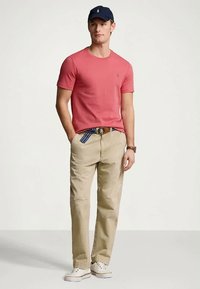 Vyriškas derinys su prigludusia koralų spalvos marškinėlių, gelsvai rudos spalvos kelnėmis su šiek tiek susidėvėjusiu efektu ir tamsiai mėlyna kepure. Dėvima su baltais sportiniais bateliais.