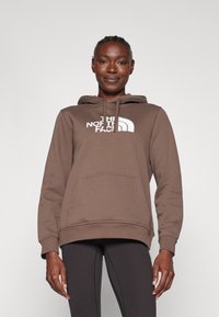 Sweatshirt castanho com um bolso frontal, capuz com cordão e logótipo branco. Textura de tecido suave, corte relaxado e punhos em ribana nas mangas.