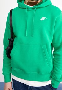 Grön hoodie i mjukt tyg, med en kenguruficka och dragsnören, och en vit Nike-logga på bröstet.