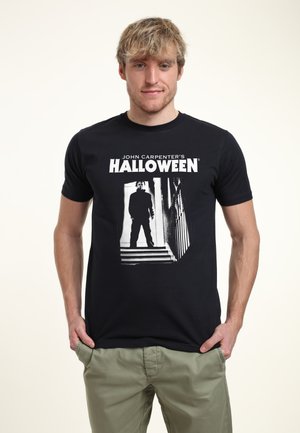 Černé bavlněné tričko s grafickým potiskem siluety postavy na schodech a textem "John Carpenter's HALLOWEEN" nad ním. Krátké rukávy.
