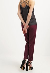 Top in satin nero con dettagli decorativi sulle spalline, abbinato a pantaloni a sigaretta bordeaux e sandali neri con tacchi alti.