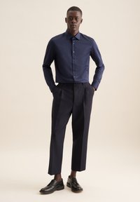 Marineblauw overhemd met een puntkraag, knopen aan de voorkant, gecombineerd met hoog ingezet zwarte broek en zwarte leren schoenen, minimalistisch ontwerp.