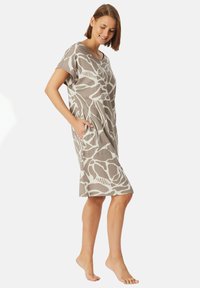 Vestido beige de manga corta con patrones abstractos blancos, a la altura de la rodilla, con bolsillos laterales y una textura de tela suave.