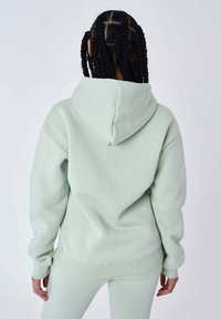 Felpa verde chiaro realizzata in morbido tessuto, con un ampio cappuccio, polsini a coste e una vestibilità rilassata. Texture liscia senza motivi o marchi visibili.